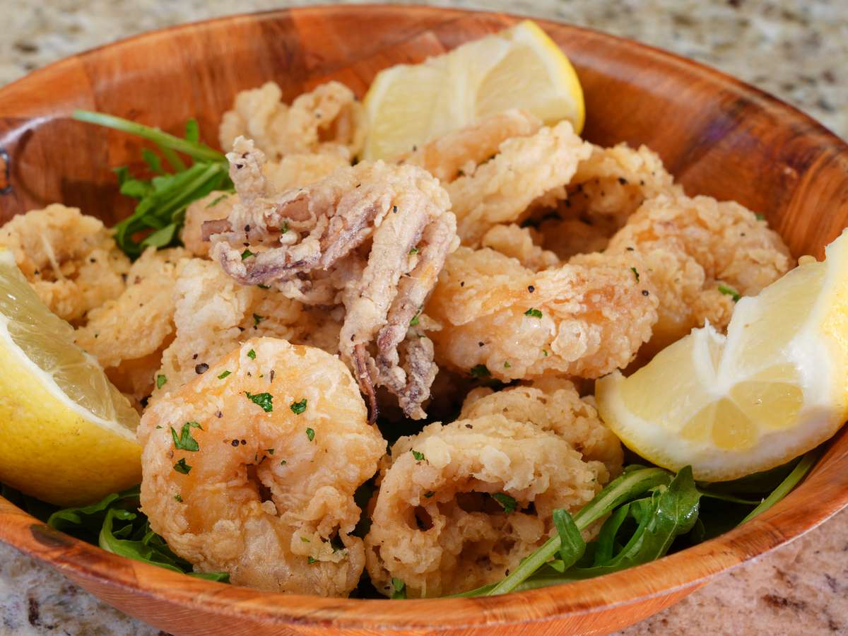 Golden fried calamari and shrimp served in a wooden bowl with lemon wedges and fresh arugula on a granite countertop.