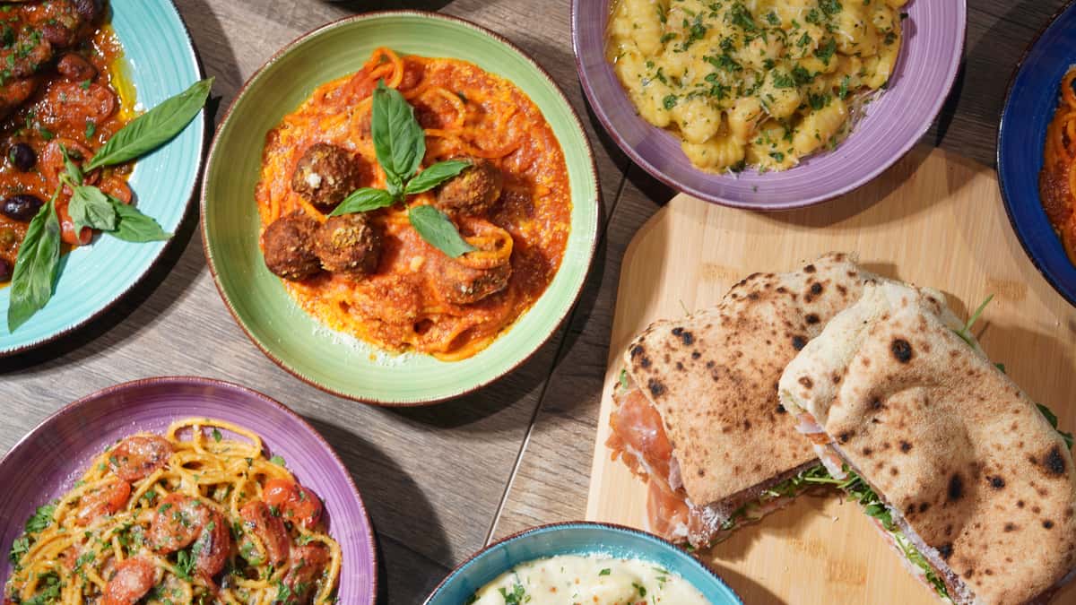 Assorted Italian dishes including pasta with meatballs, gnocchi, tomato spaghetti, and flatbread sandwich on a wooden table