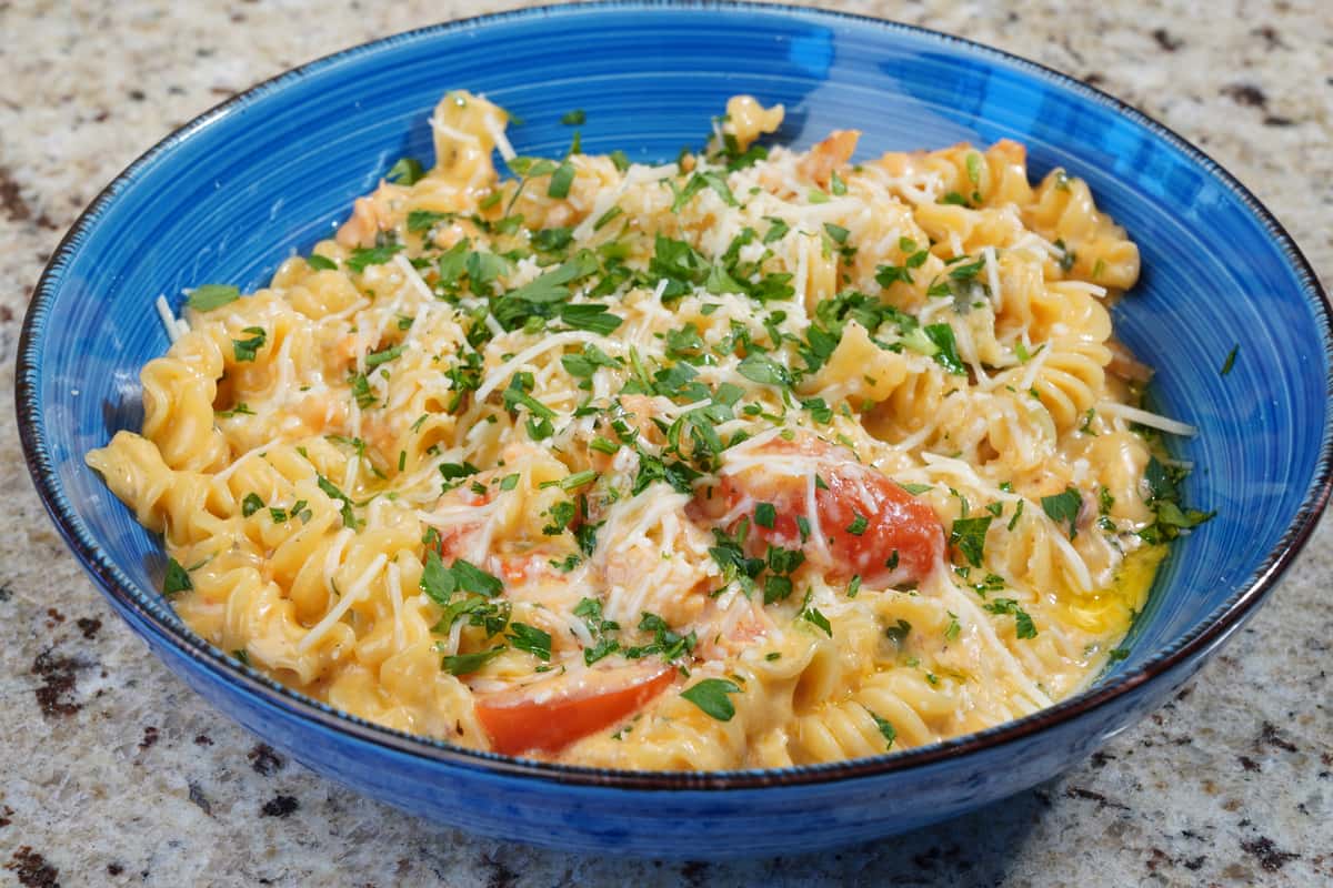 Fusilli pasta in a creamy cheese sauce with cherry tomatoes and fresh parsley, served in a blue ceramic bowl on a granite countertop