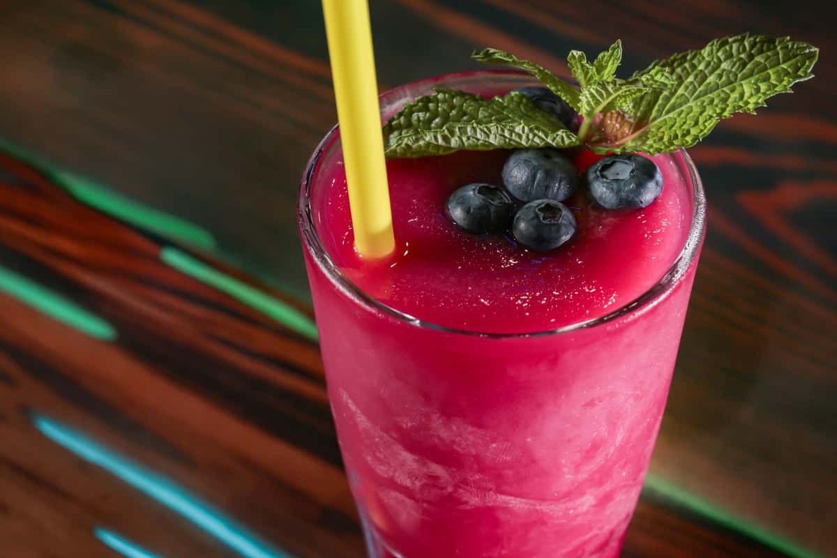 Frozen blueberry cocktail topped with fresh blueberries and a sprig of mint, served with a yellow straw.