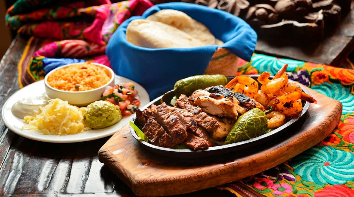 Sizzling fajitas with chicken, steak, shrimp, and bell peppers, served with rice, salsa, guacamole, and tortillas.