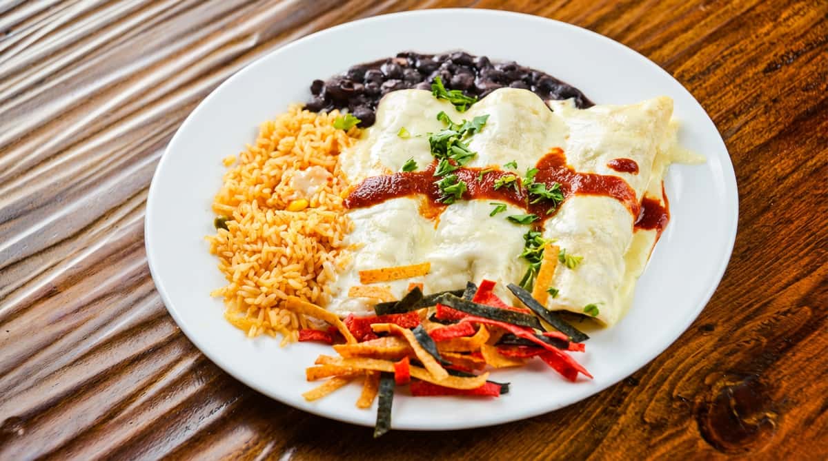 Chicken enchiladas with white sauce, red sauce, cilantro, rice, black beans, and tortilla strips on a white plate.