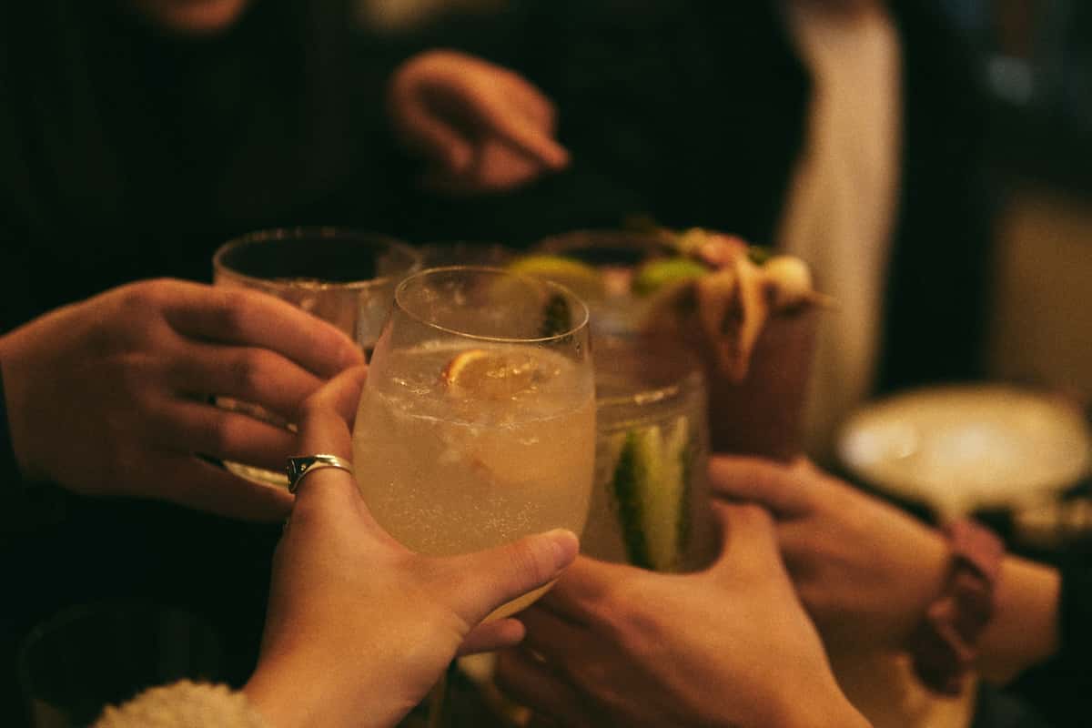 Group of friends toasting with assorted cocktails in a warm, dimly lit setting, featuring citrus and herb garnishes.