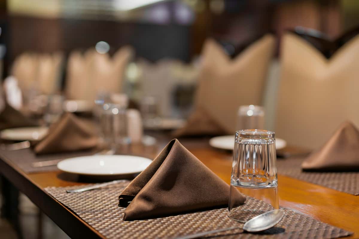 Elegant restaurant table setting with brown folded napkins, upside-down water glasses, and neatly arranged cutlery.