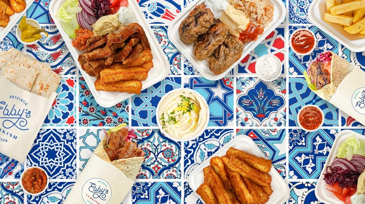 Various Turkish dishes on a white and blue patterned surface, including doner kebab, kofte, hummus, wraps, and fries.
