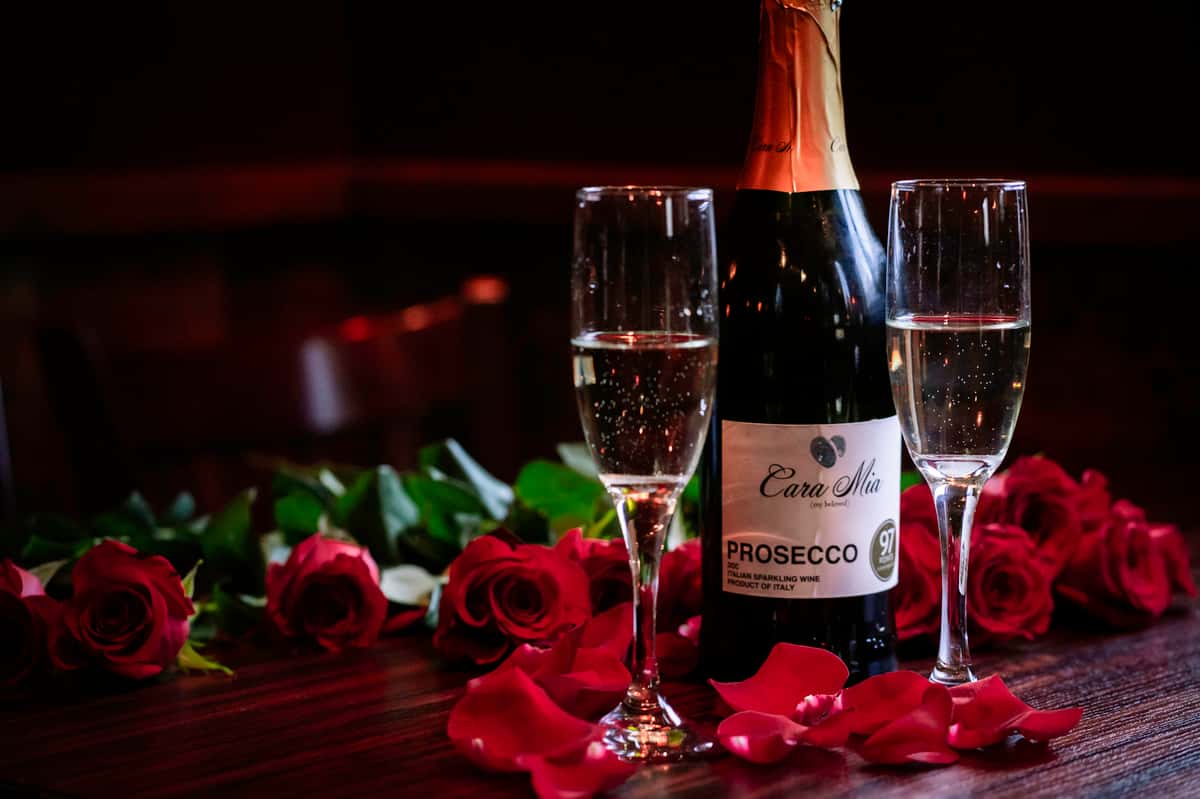 a bottle of sparkling wine with 2 glasses and roses