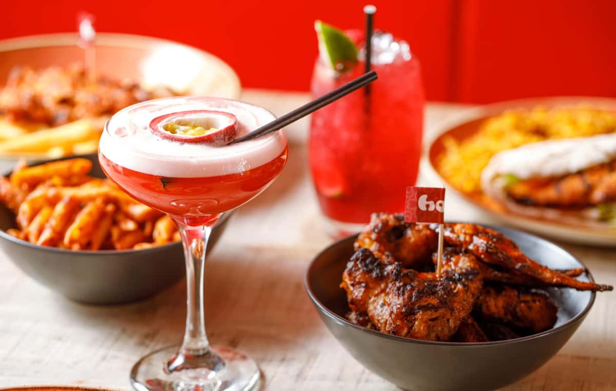 Red passion fruit cocktail with foam and garnish, served alongside grilled chicken wings, fries, and a chicken burger on a table.