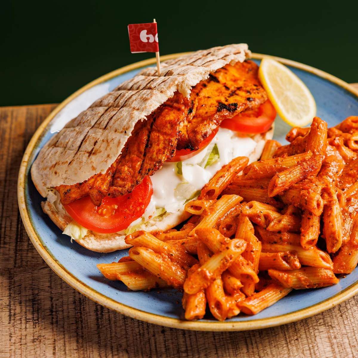 Grilled chicken pita with tomato, lettuce, and creamy sauce served alongside penne pasta in a rich tomato cream sauce