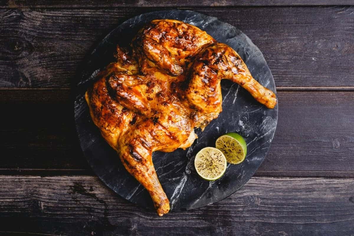 Overhead view of grilled spatchcock chicken with charred wings, lime wedges, corn on the cob, rice, and salad on rustic table