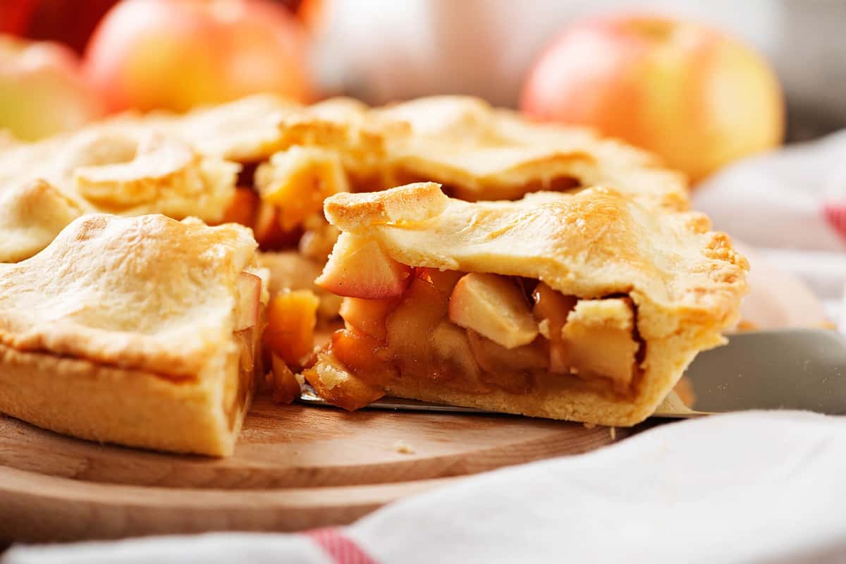 Freshly baked apple pie with a golden crust, sliced to reveal a warm, cinnamon-spiced apple filling on a wooden board.