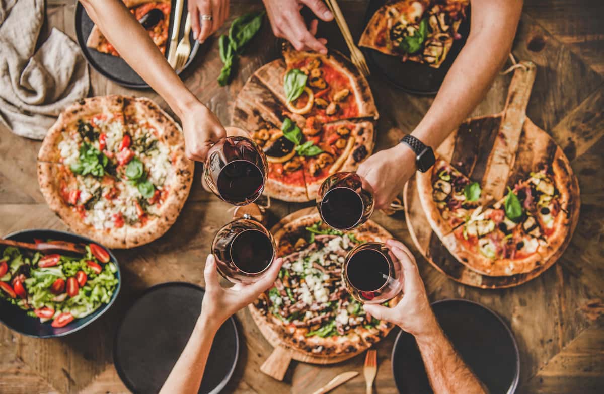 people giving a toast with several pizza on the table