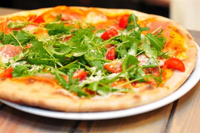 pizza with lot of greens, cheese and tomatoes