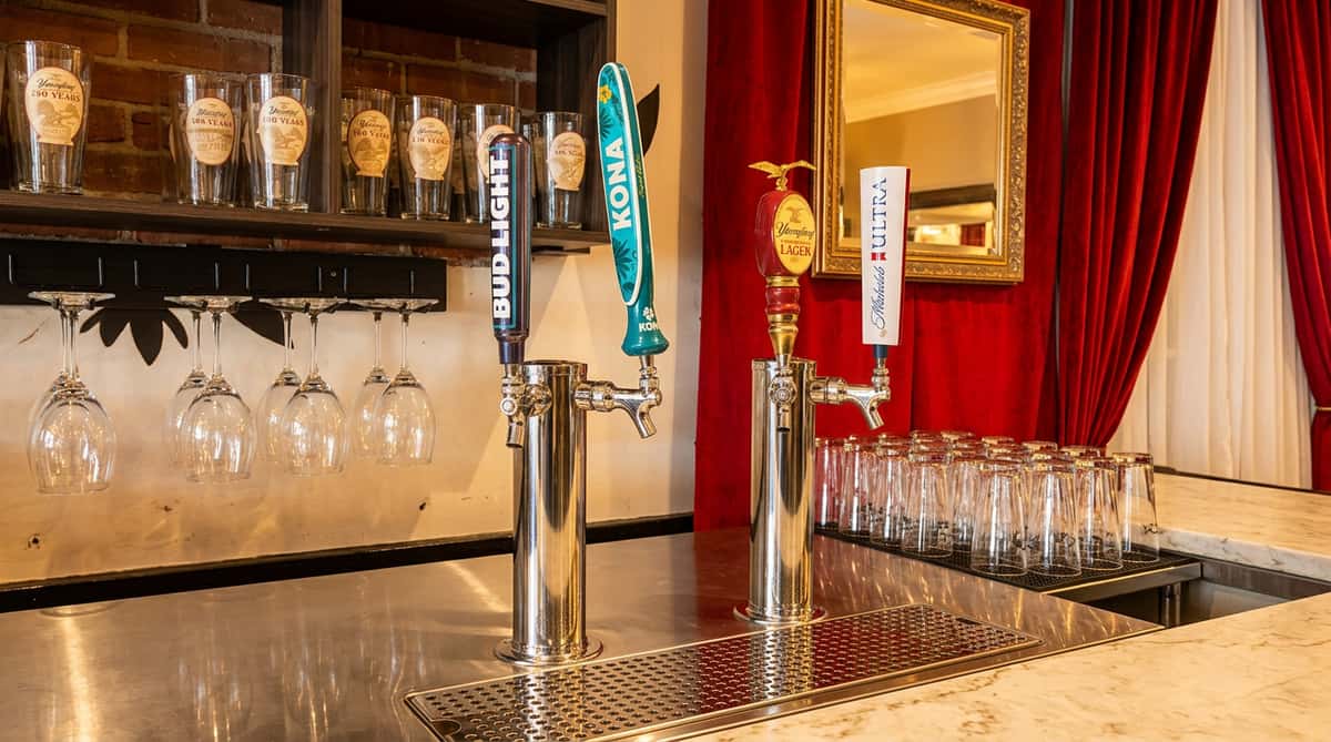 Beer taps for Bud Light, Kona, Yuengling, and Michelob Ultra on a bar, with branded glasses in the background.