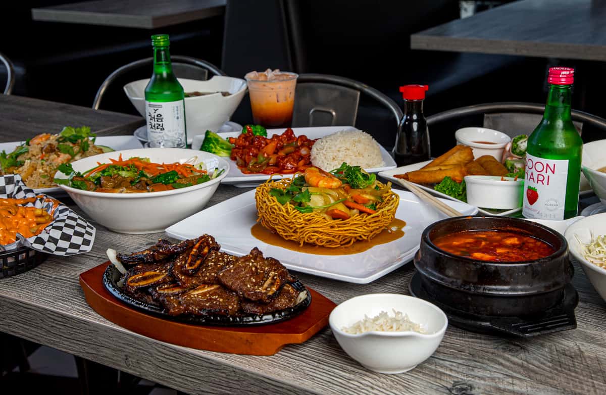 A vibrant spread of various Vietnamese dishes, including sizzling meats, stir-fries, crispy noodles, and rice, perfect for enjoying with friends at a Vietnamese restaurant in Rancho Cucamonga.