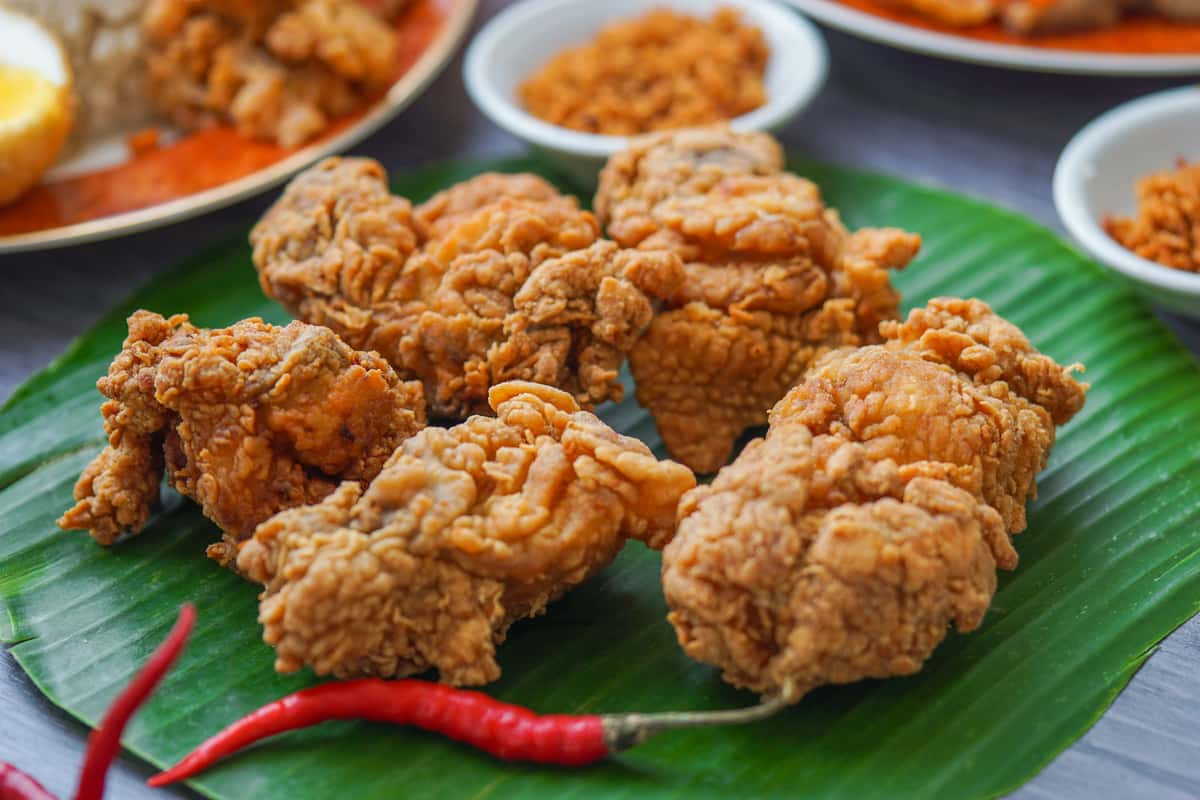 Golden crispy fried chicken pieces arranged on a banana leaf with red chili garnish, perfect for Southern comfort food or spicy street food-style dining.