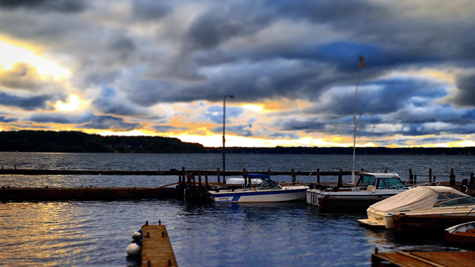 Scenic waterfront marina at sunset with docked boats under dramatic cloud-filled skies, offering a peaceful lakeside view ideal for outdoor dining or waterfront lodging experiences.