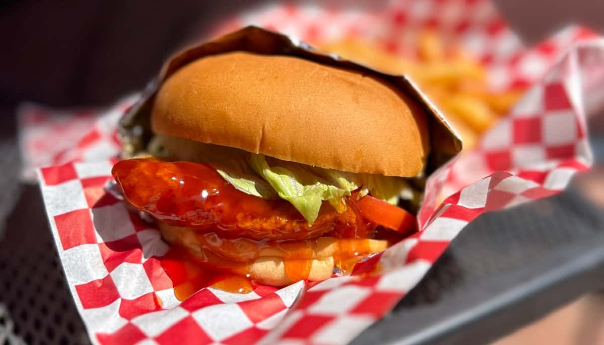 Crispy chicken sandwich with buffalo sauce, lettuce, and tomato in a soft bun, served in a red checkered basket.