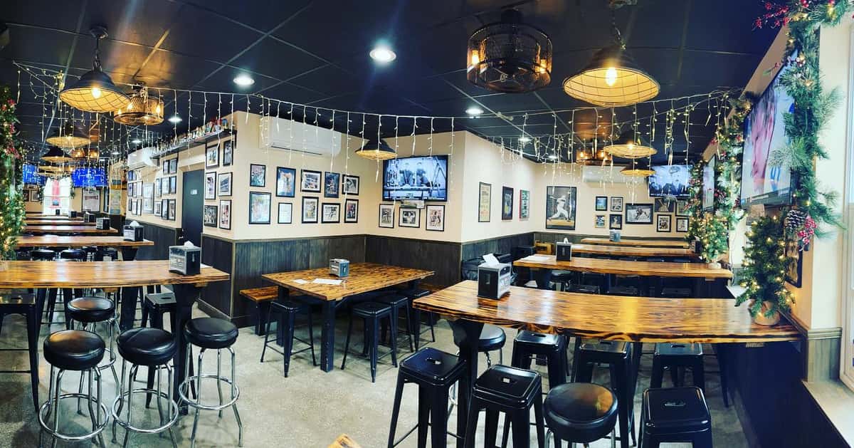 Cozy taproom decorated with holiday lights and framed sports photos, featuring wood tables, barstools, and wall-mounted TVs.