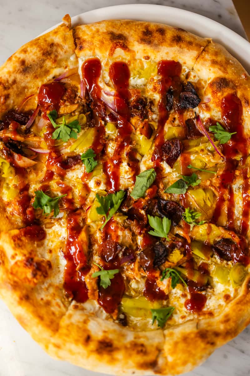 BBQ pizza topped with caramelized onions, banana peppers, fresh parsley, and barbecue sauce drizzle on a golden crust.