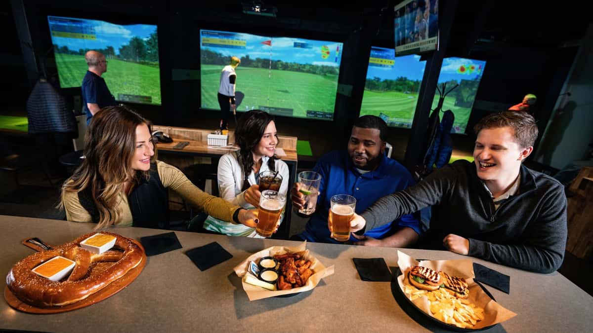 Friends toasting with beer and enjoying food at X-Golf