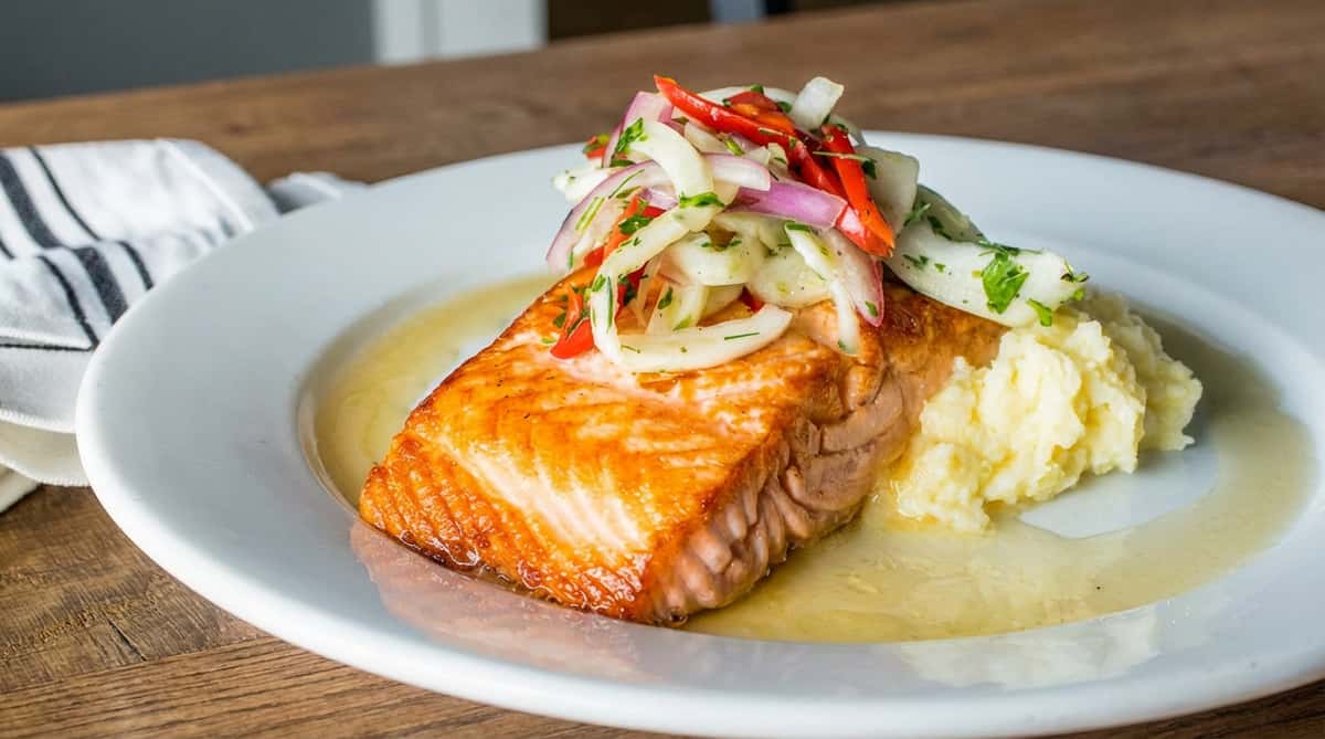 Pan-seared salmon fillet with mashed potatoes and an onion-pepper relish on a white plate