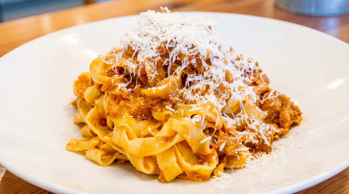 Pasta with a reddish-orange sauce and a generous topping of shredded parmesan cheese on a white plate