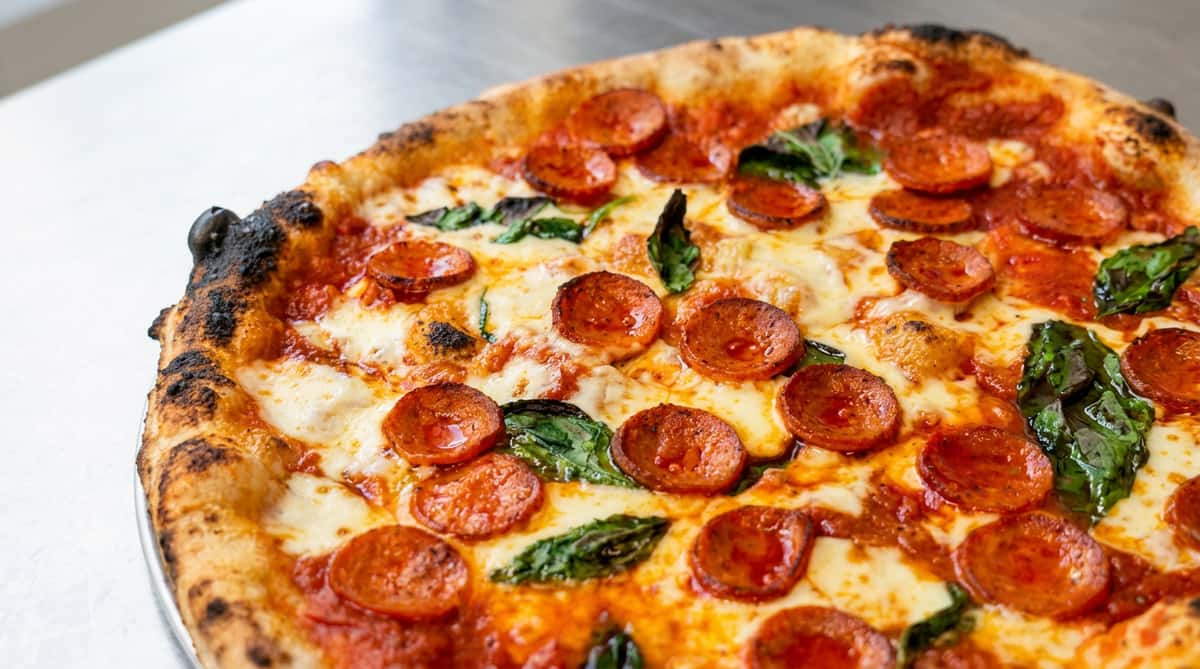 Pepperoni pizza with melted mozzarella, red sauce, green basil, and a charred crust.