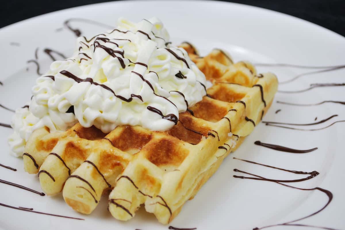 Waffles on a plate with ice cream on top and chocolate drizzle
