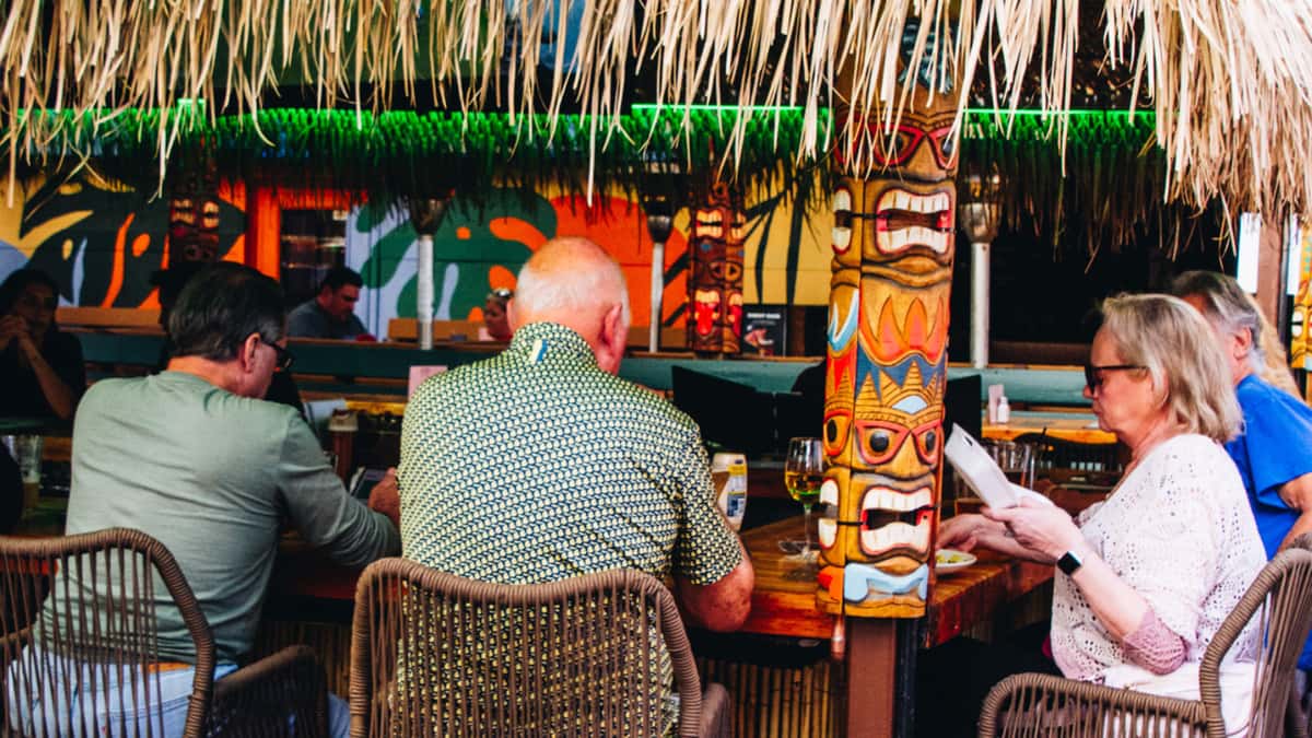 Guests dining at the tiki bar at O.H.S.O. Paradise Valley, featuring covered patio seating and colorful tiki décor.