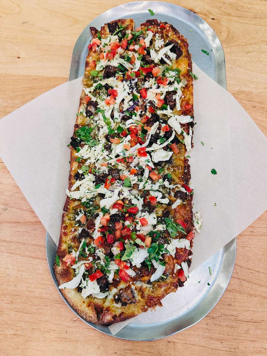 Taco pizza with chimichurri sauce, diced steak, monterey jack, cotija, slaw and pico de gallo