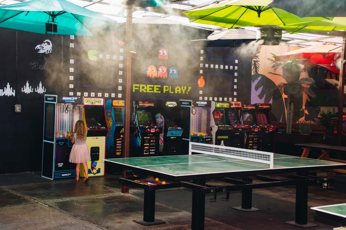 Free game zone at O.H.S.O. Paradise Valley in Phoenix, featuring arcade games, ping pong tables, shaded seating, and patio misters.