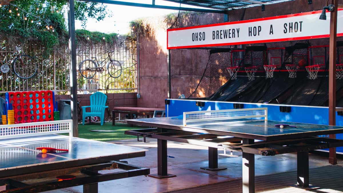 Free game zone at O.H.S.O. Paradise Valley with arcade games, ping pong tables, colorful umbrellas, and patio seating.