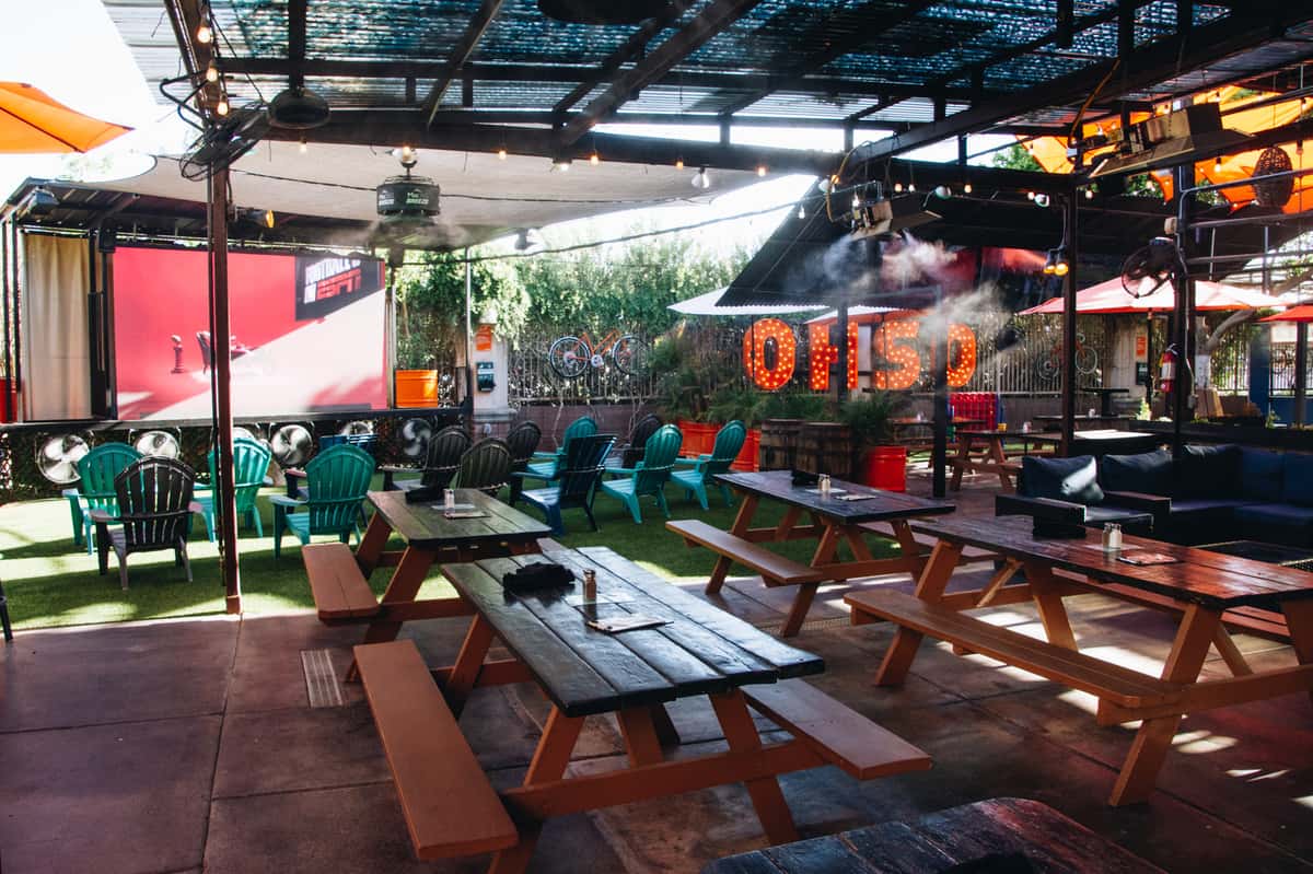 Paradise Valley patio at O.H.S.O. with big-screen TVs, shaded outdoor seating, misters, and lawn space for group events.