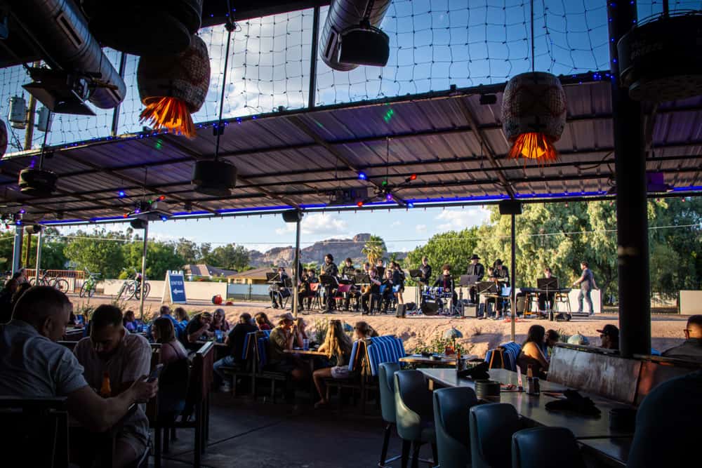 Outdoor patio space with a view of the Arizona Canal and band playing along canal. There is a view of Camelback Mountain in the back. Located in Arcadia neighborhood in Phoenix Arizona at OHSO Party House.