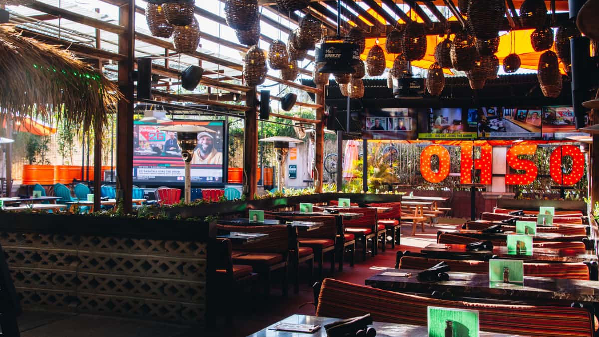 Covered outdoor patio at O.H.S.O. Paradise Valley with group seating, multiple TVs, misters, and the illuminated O.H.S.O. sign.