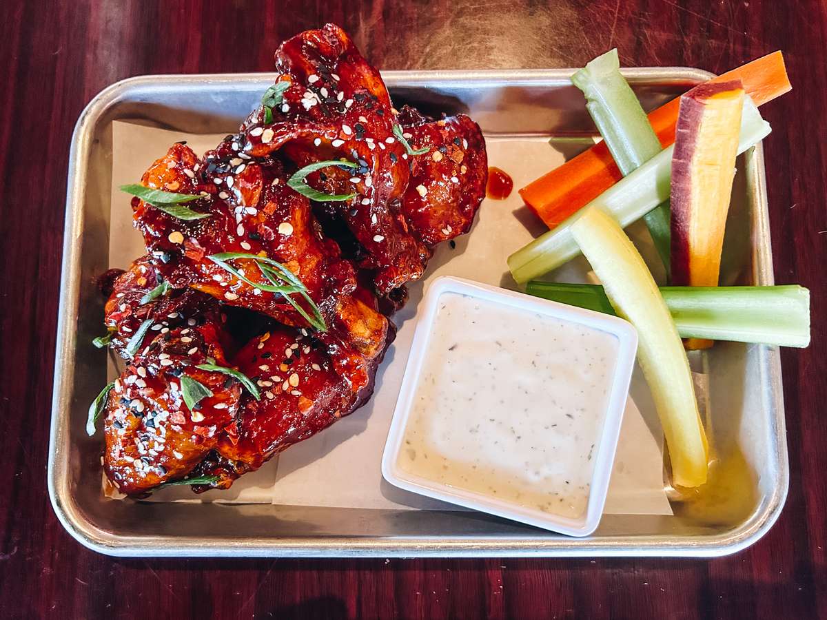 Gochujang glazed wings with sesame seeds, chile flakes and green onions, served with carrots, celery and ranch