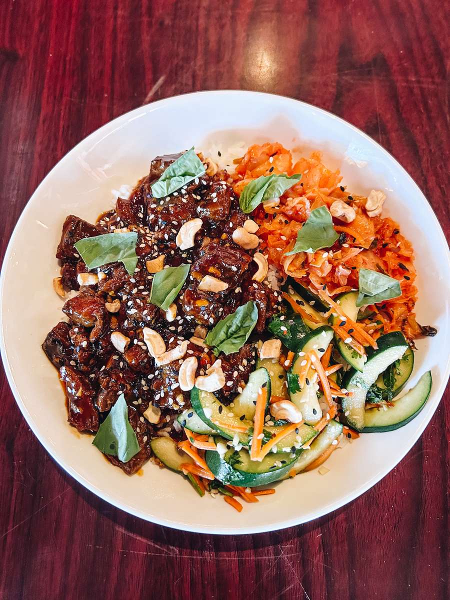 Beef bulgogi bowl with rice, cucumber salad, kimchi, gochujang sauce, basil, sesame seeds and cashews