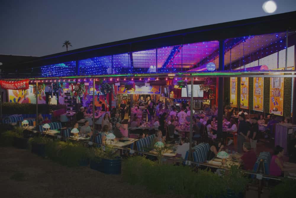 Exterior of O.H.S.O. Party House in Arcadia at night, with guests dining and gathering throughout the colorful indoor-outdoor private event space.