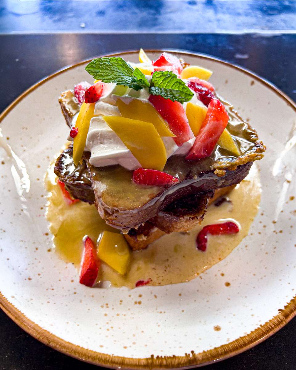 Tres leches French toast topped with bourbon ginger glaze, whipped cream, mango, strawberries and mint
