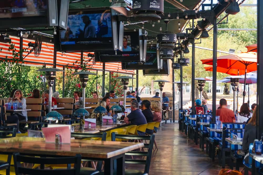 Covered patio at O.H.S.O. Sunnyslope in Phoenix with group seating, TVs, string lights, fans, and misters.