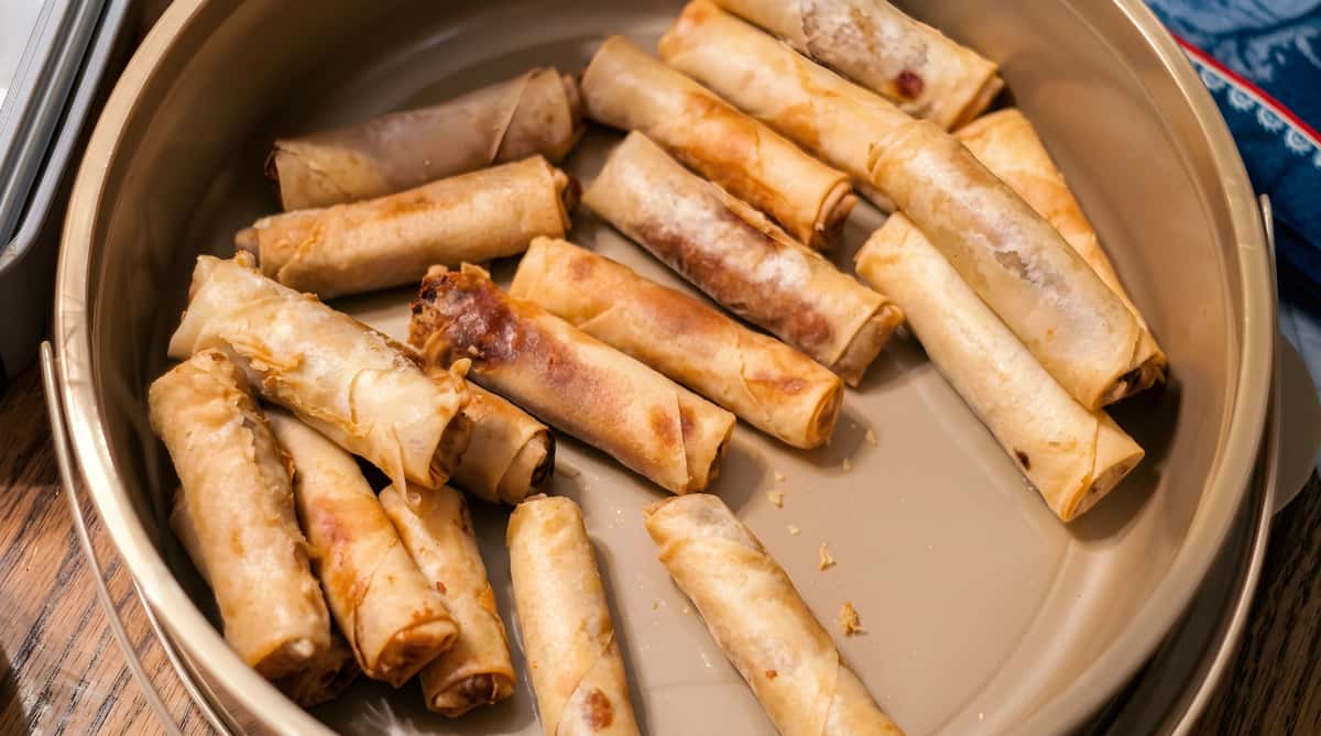 A platter of golden-brown lumpia (Filipino spring rolls) with some showing dark filling, on a tan tray.