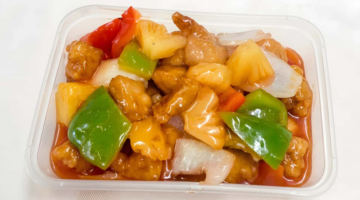 Sweet and sour chicken with red bell pepper, green bell pepper, onion, and pineapple chunks in a rich orange sauce.
