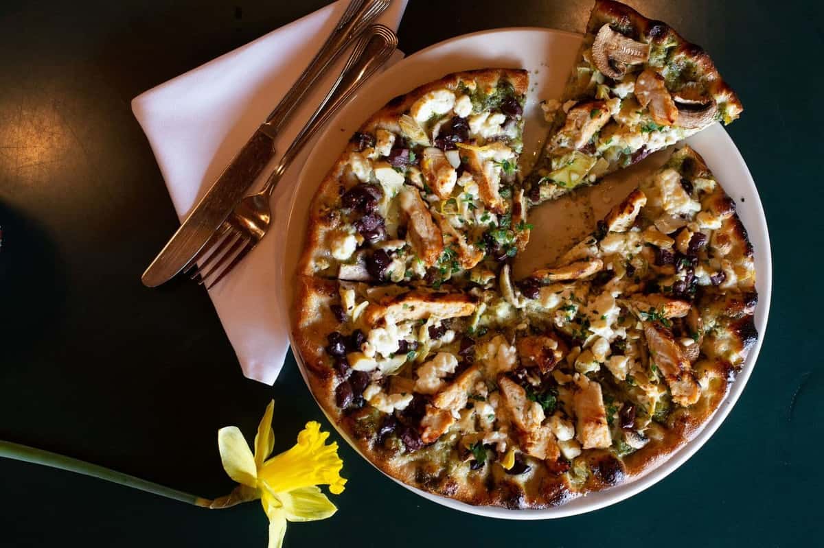 rustic Italian pizza topped with fresh herbs, melted cheese, and savory ingredients, served on a wooden board for a warm, artisanal presentation.