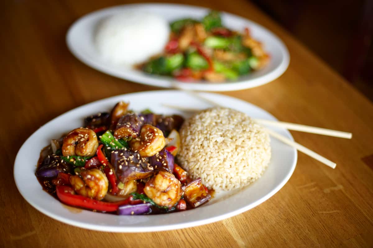 Garlic shrimp with eggplant, bell peppers, and brown rice in the foreground; chicken and vegetables with white rice in the background.