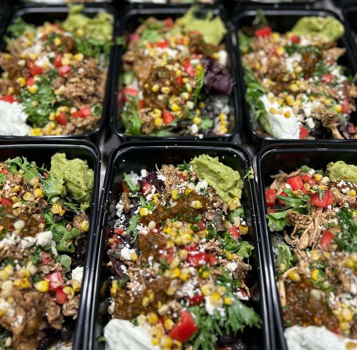 Fresh salads in takeout containers topped with pulled chicken, corn, guacamole, salsa, tomatoes, and cilantro.
