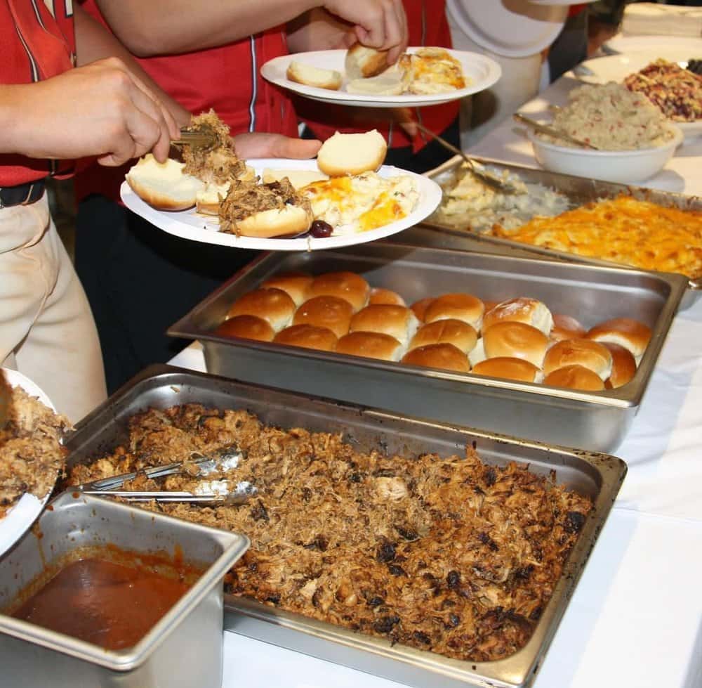 Guests serving themselves pulled pork, mashed potatoes, and rolls from a buffet setup.