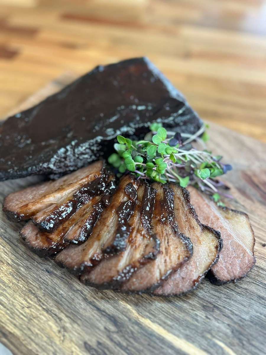 A plate of tender, sliced smoked brisket glazed with a rich sauce, garnished with fresh microgreens.