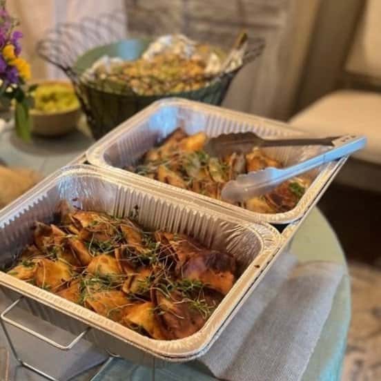 Aluminum trays filled with baked stuffed pasta topped with herbs, set on a buffet table with tongs for serving.