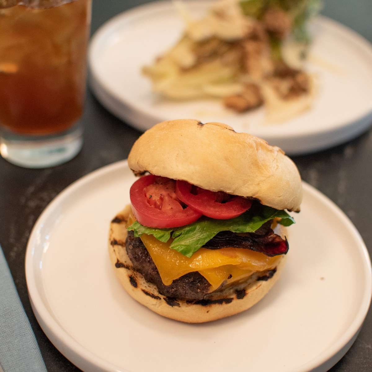 A grilled burger with melted cheddar cheese, lettuce, tomato, and a toasted bun.