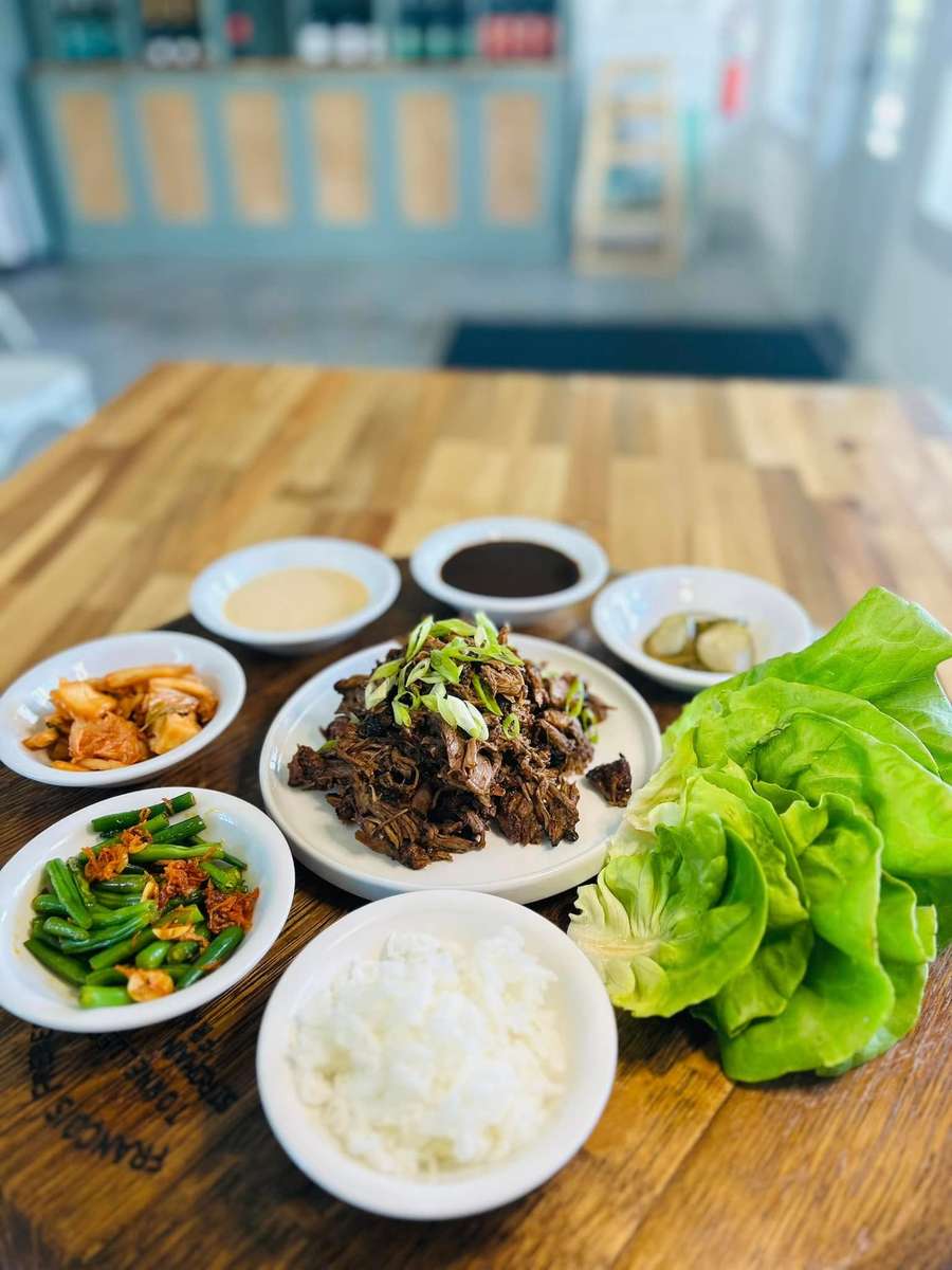A Korean BBQ meal with shredded beef, lettuce wraps, kimchi, green beans, rice, sauces, and pickled vegetables.